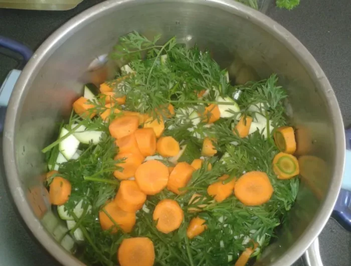casserole avec une preparation pour une soupe avec des fanes de carottes et des carottes decoupees