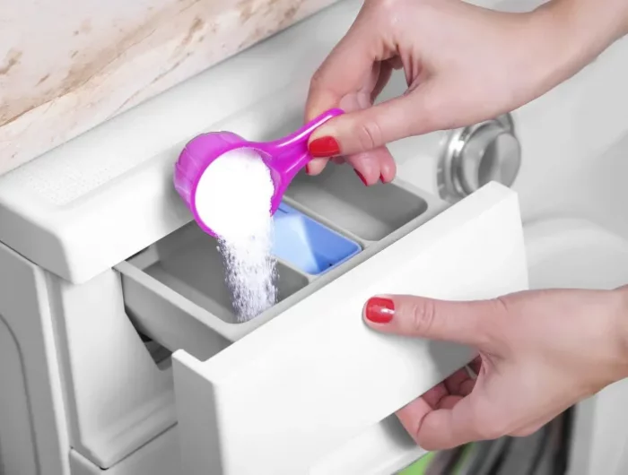 feuille de laurier dans la machine alaver une main met du detergent dasns le lave lessive
