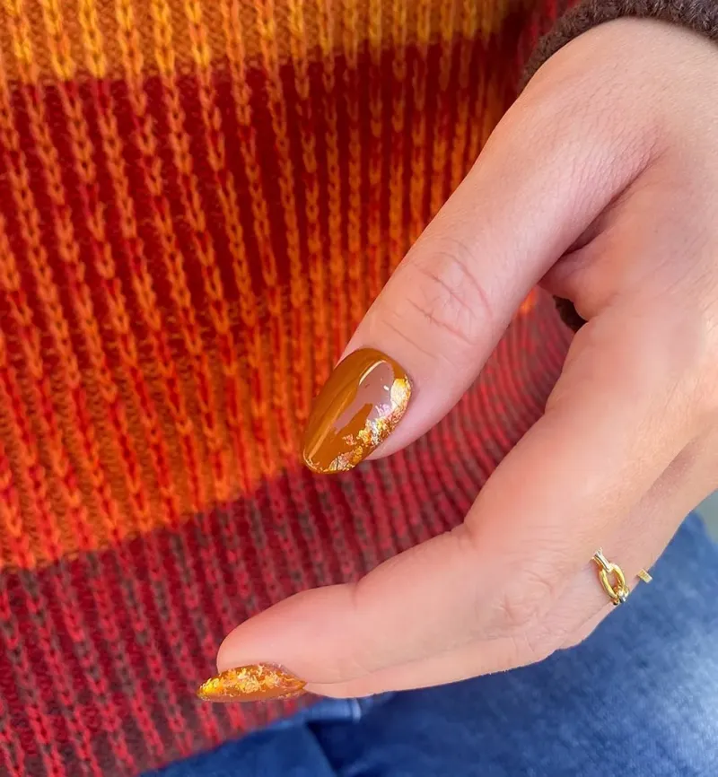 foil or sur ongles vernis de couleur orange automne sur fond de pull rouge jaune orange