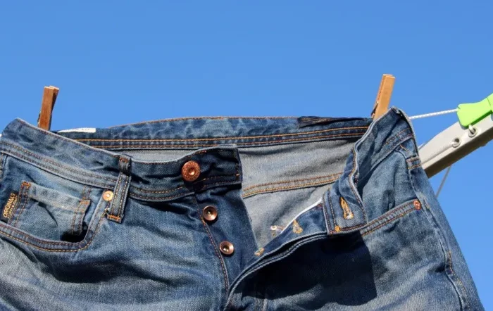 jeans deboutonne avec deux pinces a linge sur un etendoir dehors sur fond de ciel bleu