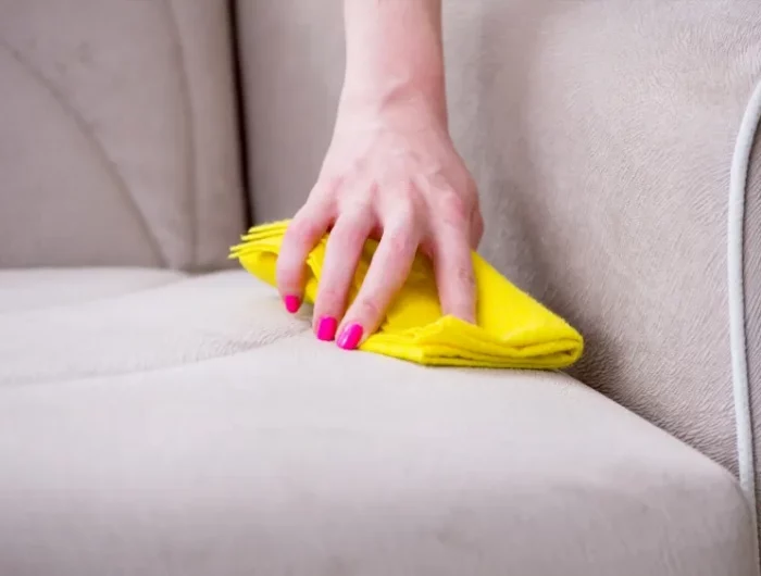 main nettoyant un canape en tissu avec un choffon jaune