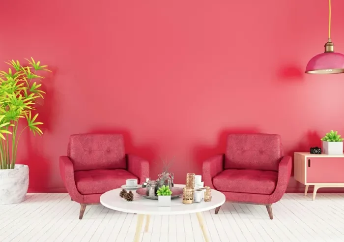 mur rouge avec deux faiteuils rouges derriere une table basse blanche et une plante verte