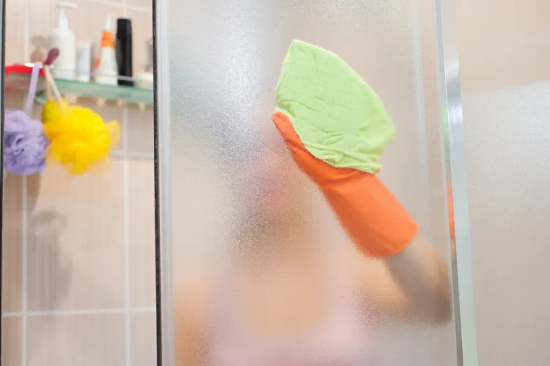 nettoyer les paroies de la douche avec des gants oranges et chiffon vert