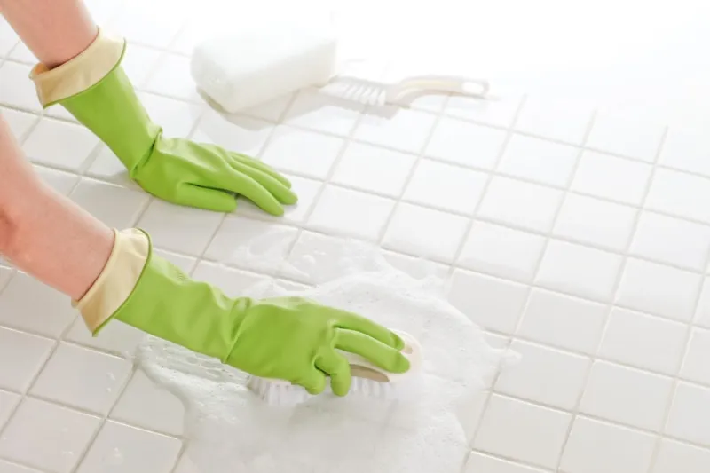 nettoyer un carrelage neuf après travaux femme aux gant verts frotte le sol blanc