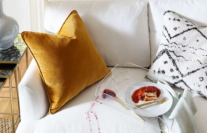 un canape blanc tache de vin rouge avec un plateau et une assiette et un coussin jaune