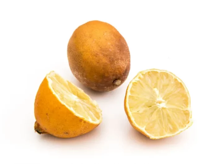 un citron entier pourri deseche et un autre decoupe en deux sur fond blanc