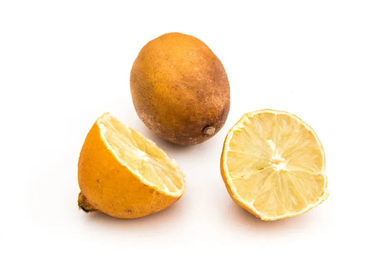 un citron entier pourri deseche et un autre decoupe en deux sur fond blanc