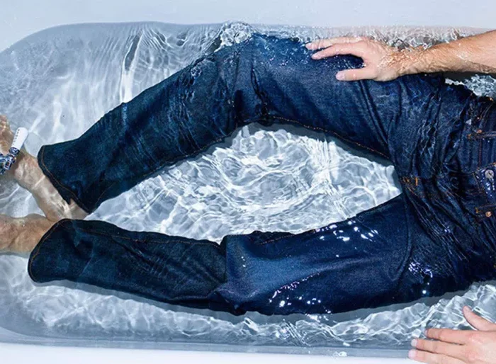 un homme portant un bleu jeans plonge dans une baignoire pleine