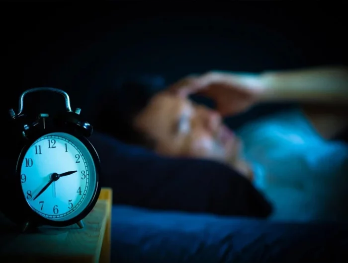 un horloge mecanique en premier plan et une personne avec une insomnie en arriere plan flou