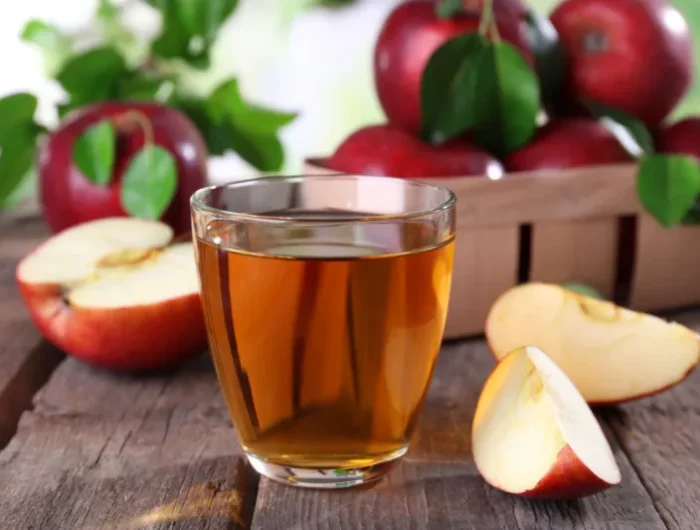 un verre pleine de jus de pommes avec des pommes découpees et des pommes rouge au fond