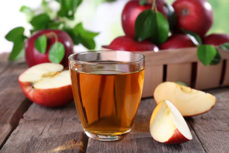 un verre pleine de jus de pommes avec des pommes découpees et des pommes rouge au fond