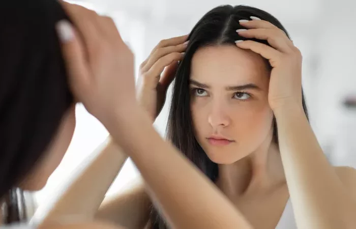 une femme brune regarde ses cheveux de pres dans un miroir