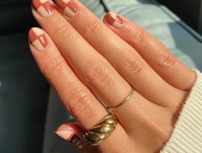une main avec les doigts avec des bagues et ongles vernis de couleurs automne dans une geometrie en contraste