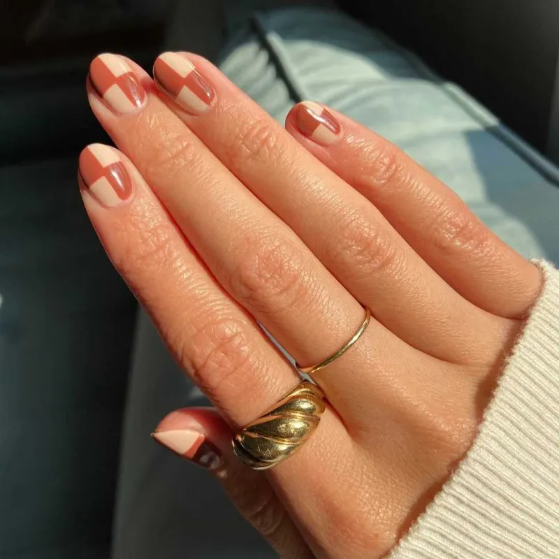 une main avec les doigts avec des bagues et ongles vernis de couleurs automne dans une geometrie en contraste