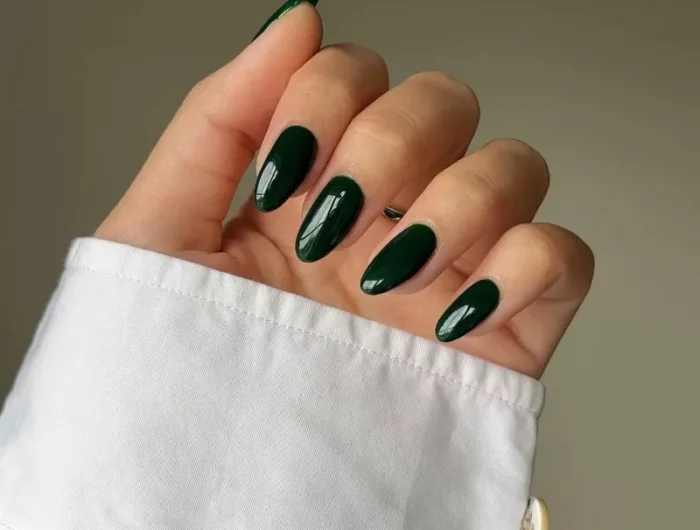 une maine avec ses ongles vernis de couleur vert fonce et une manche blanche
