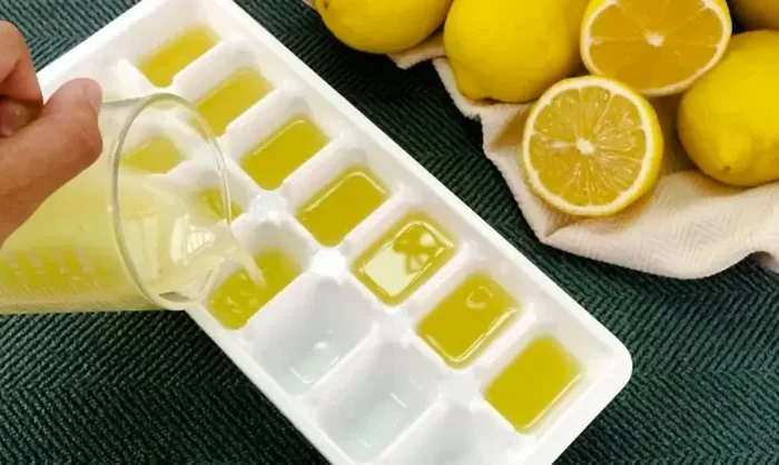 verser du jus de citron dans un bac a glacons blanc avec de citron coupes et entier en haut a droite