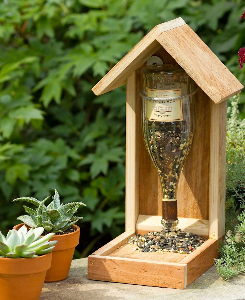 bouteille de vin remplie de grains a oiseaux accrocher a une mengeoire en bois et deux petits pots a gauches