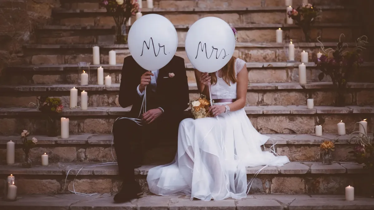 couple assis sur un escalier le jour de son mariage se cache derriere des ballons