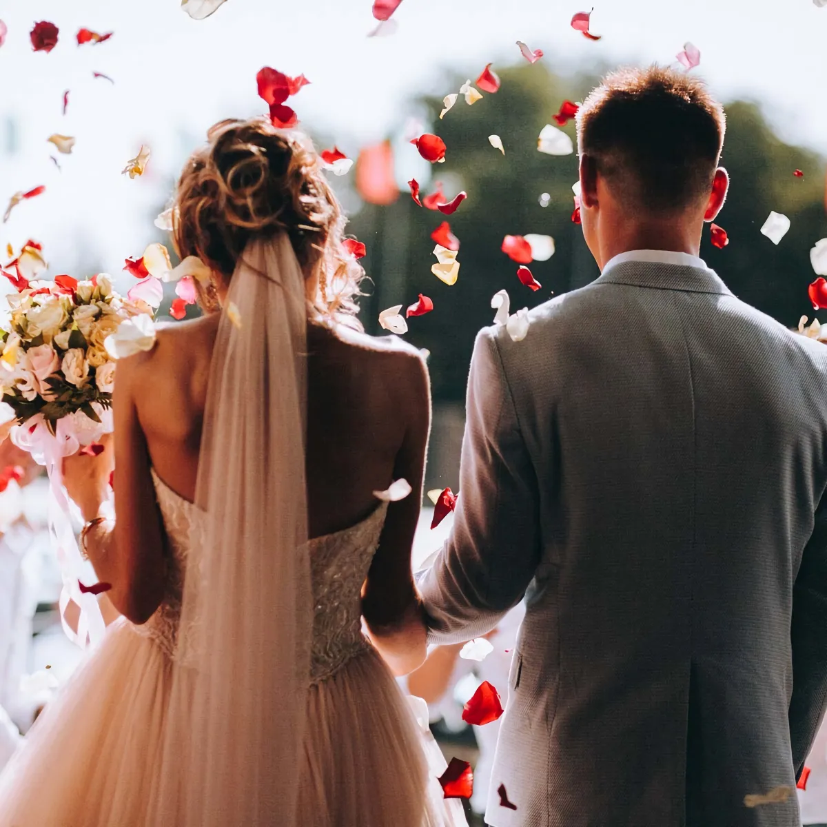 couple de dos le jour de son mariage sur fond de petales de roses de couleur rouges blanches roses et creme