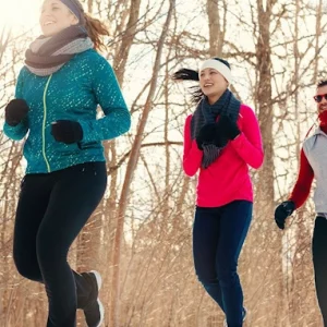 jogging entre amis dans le froid avec deux femmes en premier plan et un homme derriere elles sur fond un bois en hiver