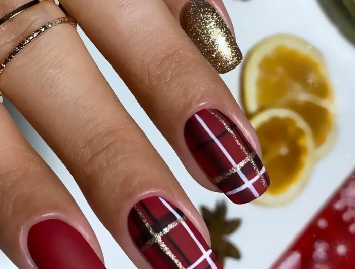 ongles noel rouges et un dore scentillant avec deux dessins sur deux ongles de lignes en grille blanches noires et dorees