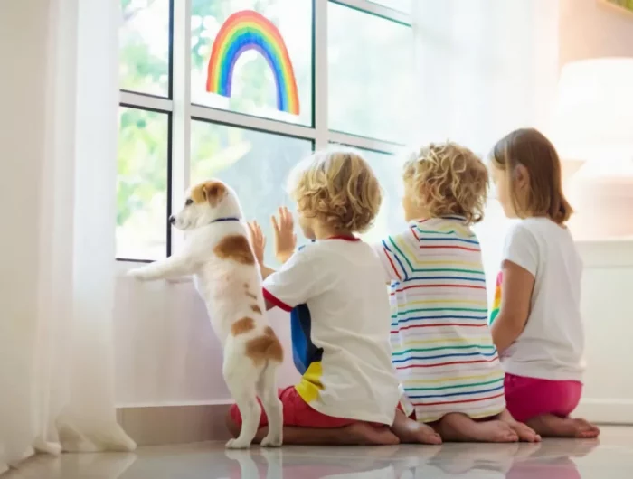 trois enfants avec un petit chien regardent par la fenetre assis sur un sol brillant dans un interieur blanc
