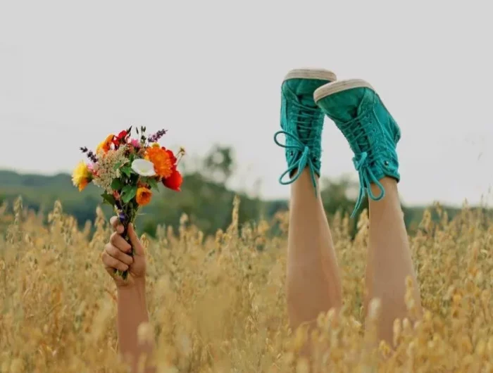 un champs avec un bras qui tient un bouquet de fleurs et deux pieds avec des chaussures vertes