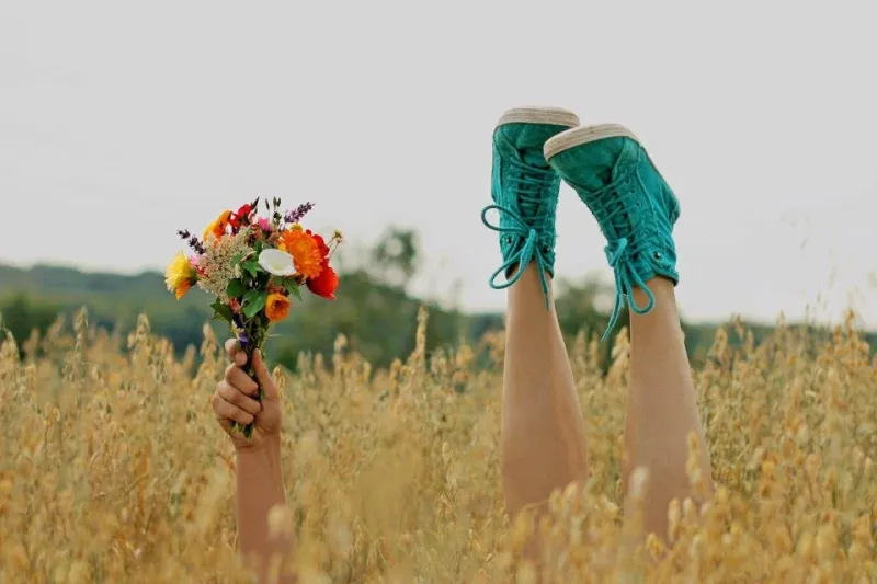 un champs avec un bras qui tient un bouquet de fleurs et deux pieds avec des chaussures vertes