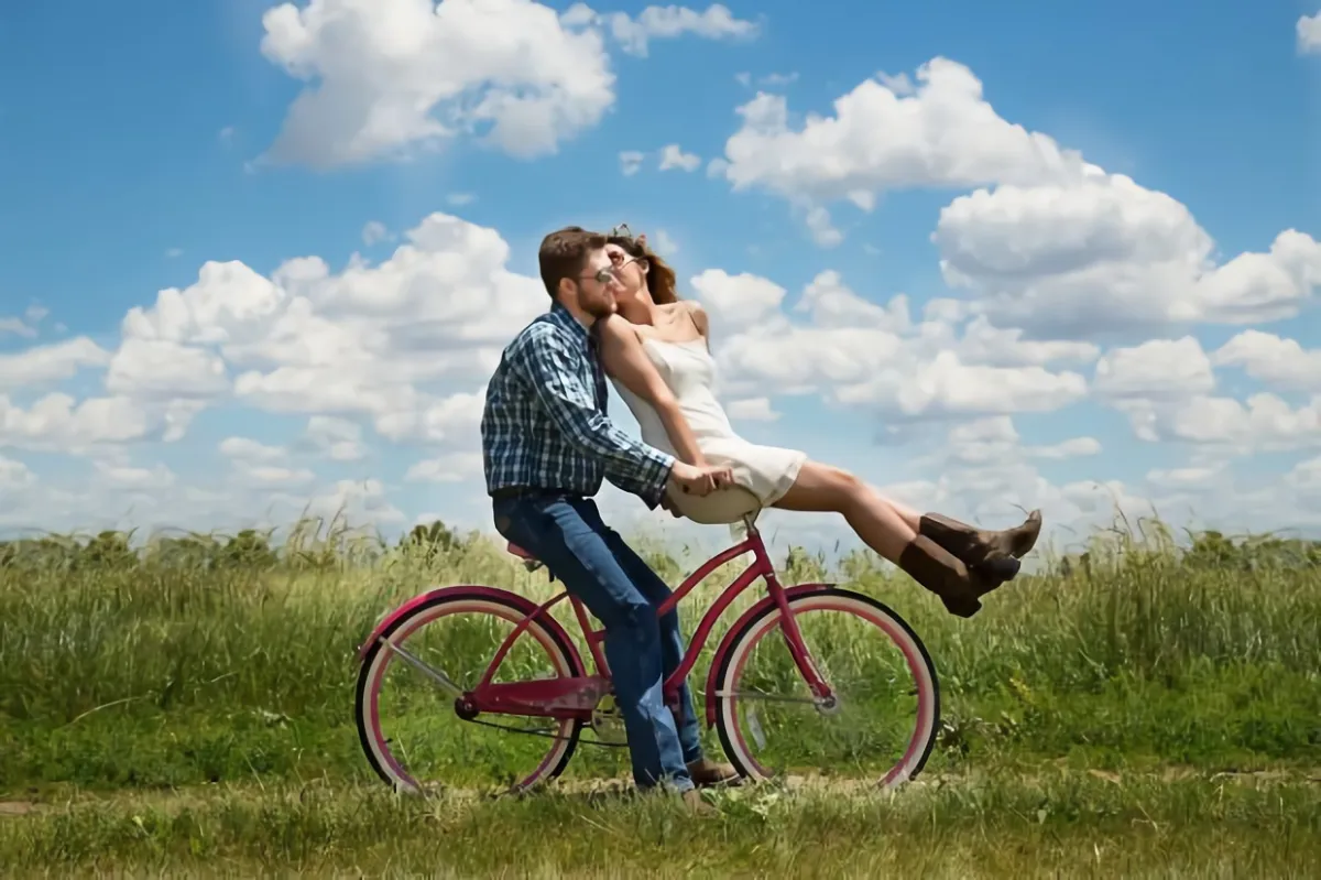 happy couple riding bicycles in the field on the background of the blue sky with white clouds
