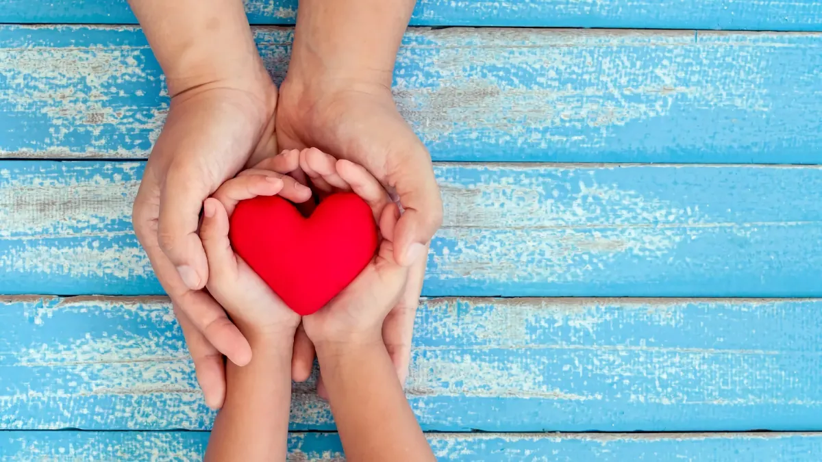 une relation saine et durable avec la symbolique du coeur rouge que deux mains le tiennent sur un fond en lattes de bois bleu ciel