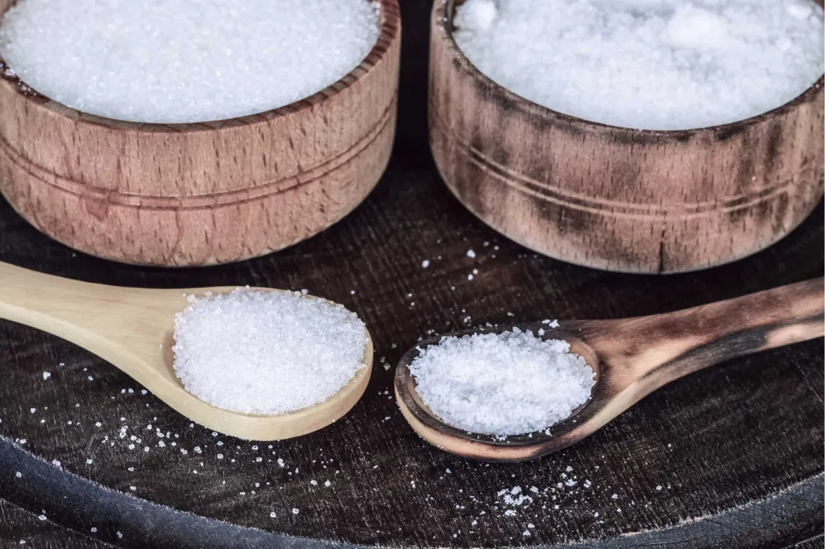 du sel et du sucre dans des bols en bois avec deux cuilleres en bois en premier plan
