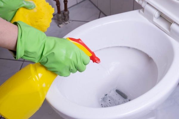 cleaning lady in the bathroom washes the toilet in green gloves and with detergent