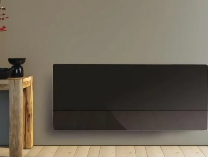 panneau rayonnant noir installe sur un mur avec une table en bois a gauche