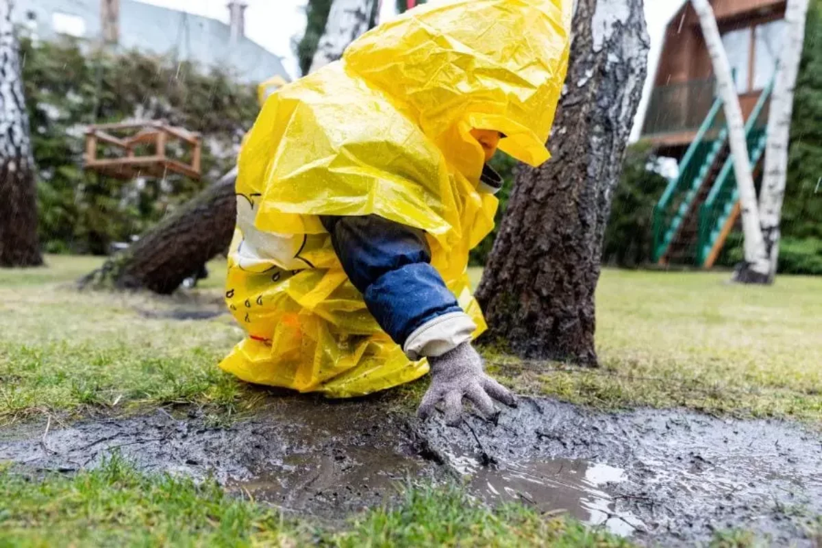 un enfant avec veste jaune qui joue dans la boue