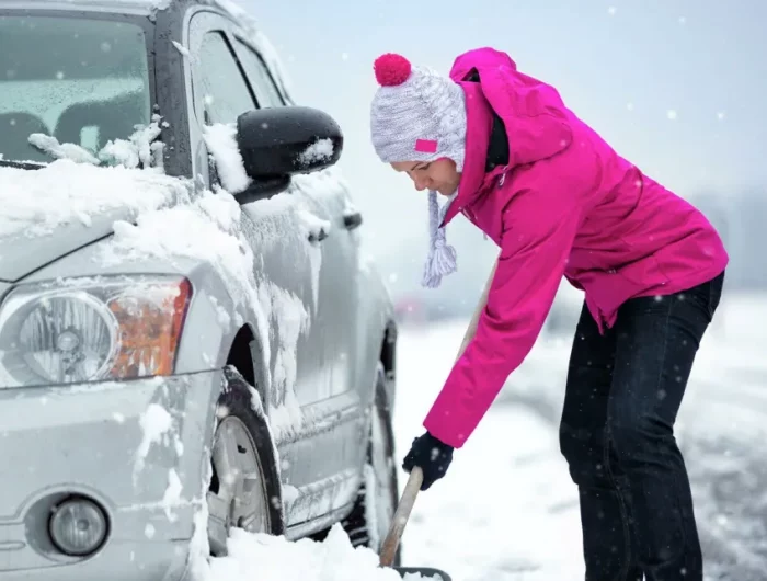 une femme en veste fuchsia qui degage sa voiture de la neige garee pres de la rue