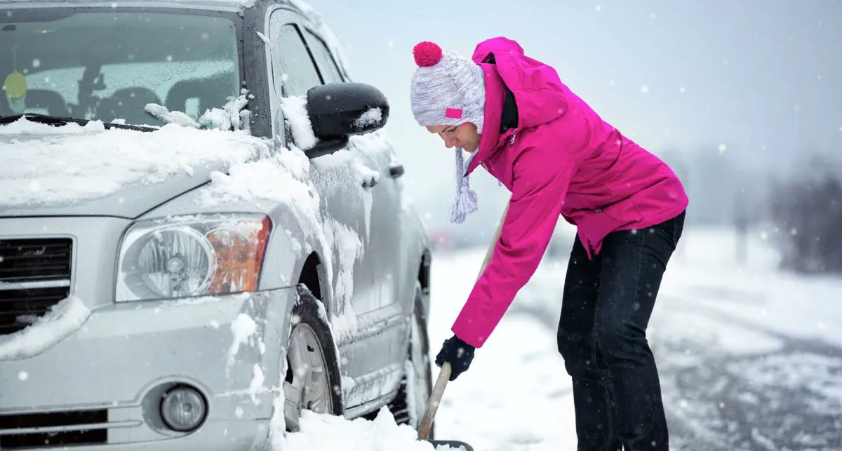 une femme en veste fuchsia qui degage sa voiture de la neige garee pres de la rue