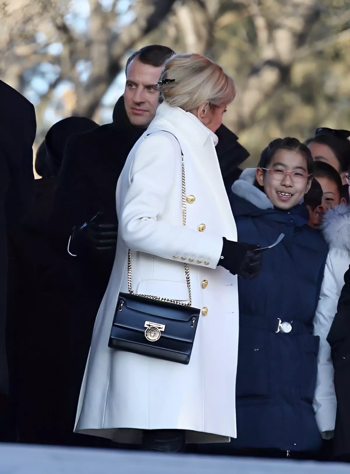 brigitte macron avec un manteau blanc et un sac noir dans un evenement public