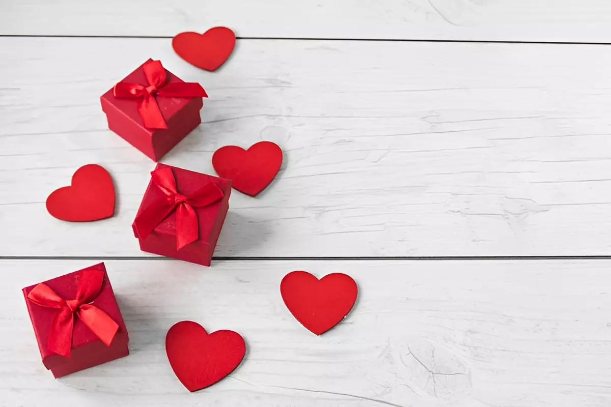 trois boites de cadeaux rouges avec des cœurs rouges autour sur fond de planches en bois peintes en blanc