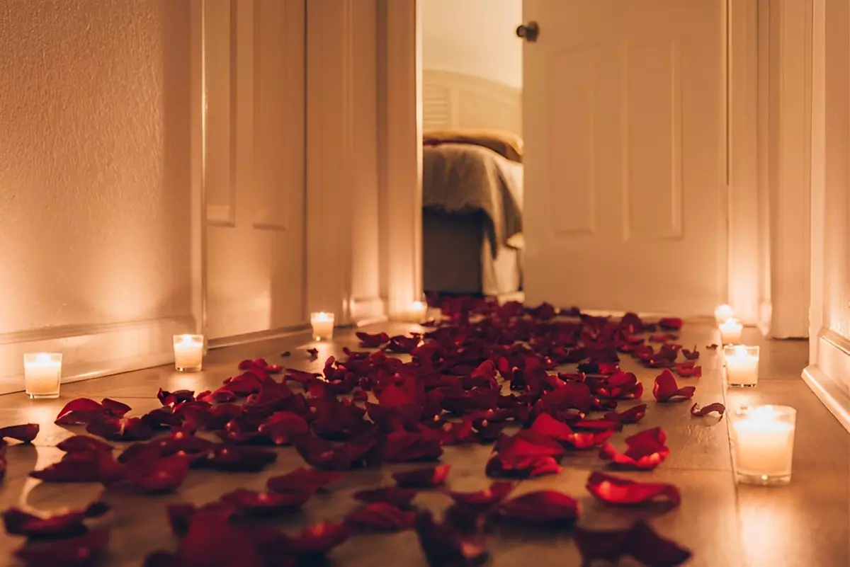 un couloir dans un appartement parceme de petales de roses rouges soulignees avec des bougies allumees sur les deux cotes menant a une chambre a coucher