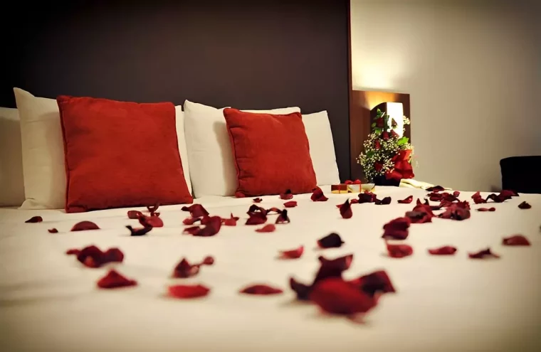 un lit couvert de petales de roses rouges avec des draps blancs et deux coussins rouges