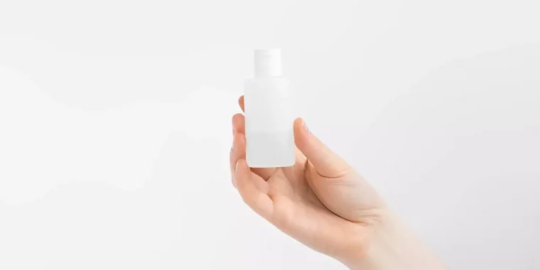 une main tient un dissolvant pour les ongles dans une petite bouteille en plastique