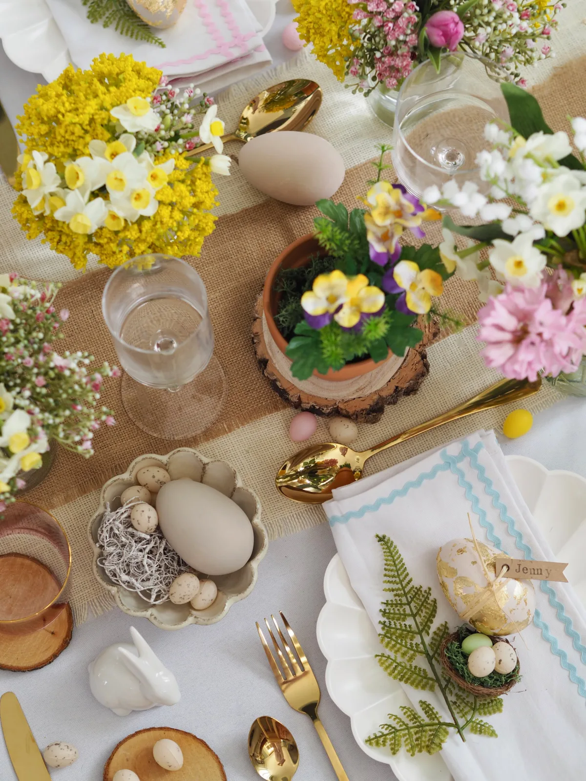 Mesa de Pascua con muchos arreglos florales campestres y flores de primavera en huevos de Pascua estampados en latón