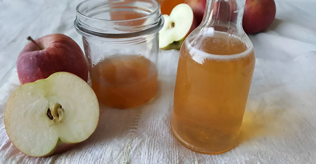 vinaigre de cidre dans une petite bouteille en verre et un bocal ouvert au milieu entpures de pommes entieres et coupees a moitie