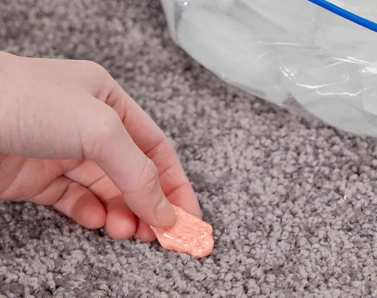 chewing gomme entre les doigts d une main sur un tapis beige et un sac plastique avec des glacons