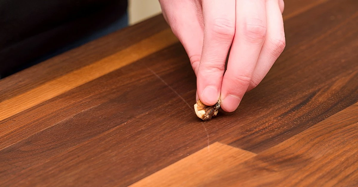 des doigts qui tiennent une noix pour traiter une rayure sur bois