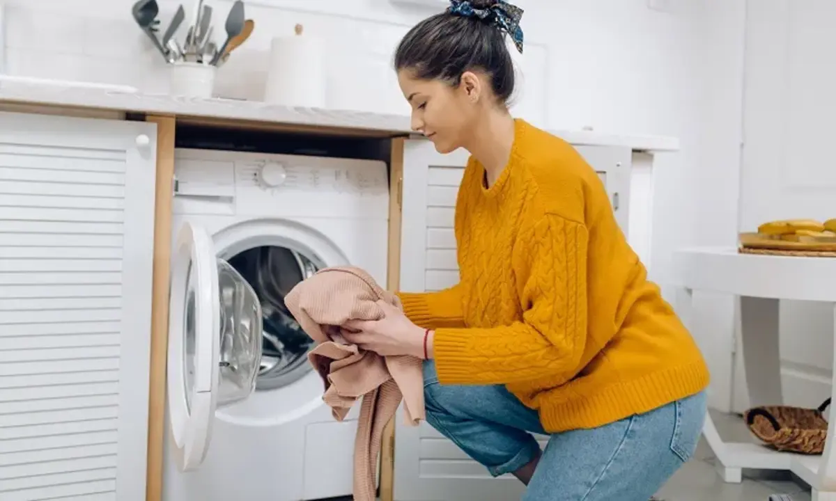 femme avec un pull jaune chargeant sa machine a laver vetements delaves