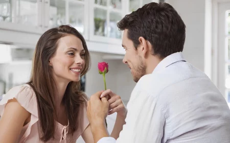 un homme en chemise blanche assis de dos offre une rose rouge a une femme qui le regarde dans les yeux et lui sourit