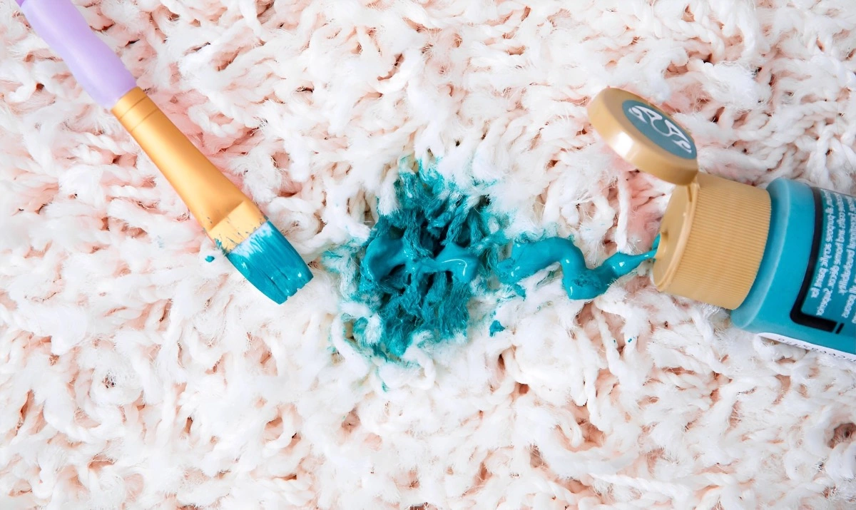 un pinceau et un tube de peinture bleue renversee sur un tapis tres claire