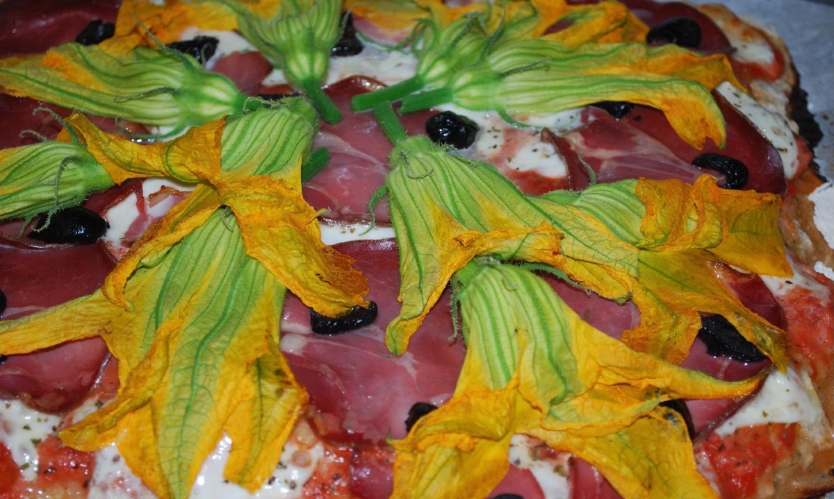 fleurs de courgette sur une pizza avec du jambon fromage sauce tomate et des olives noires