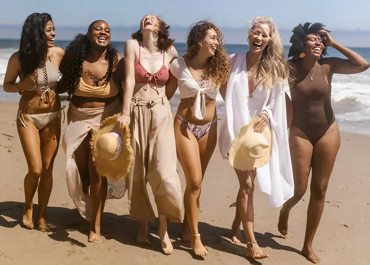 six femmes qui rient a la plage en maillots de bain accessoirises
